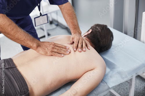 Male patient lying on couch while medical advisor making special therapeutic back massage