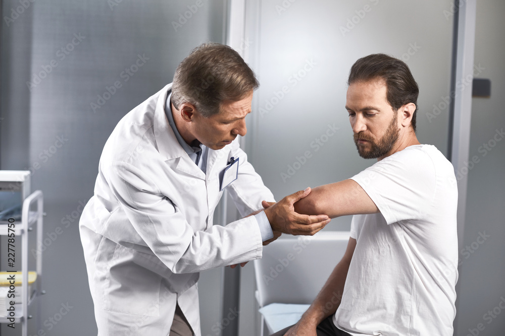 Waist up portrait of doctor testing flexion of elbow joint of patient and testing for any discomfort Waist up portrait of doctor testing flexion of elbow joint of patient and testing for any discomfort