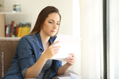 Serious woman reading a letter on a couch