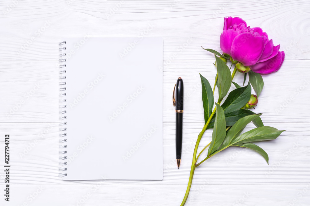 Naklejka premium Empty notepad with place for text, pen and peony flower on a white wooden background. Mockup for your design. View from above.