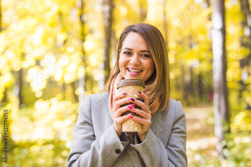 Autumn  nature and people concept - Young beautiful woman in blue coat holding a cup of coffee
