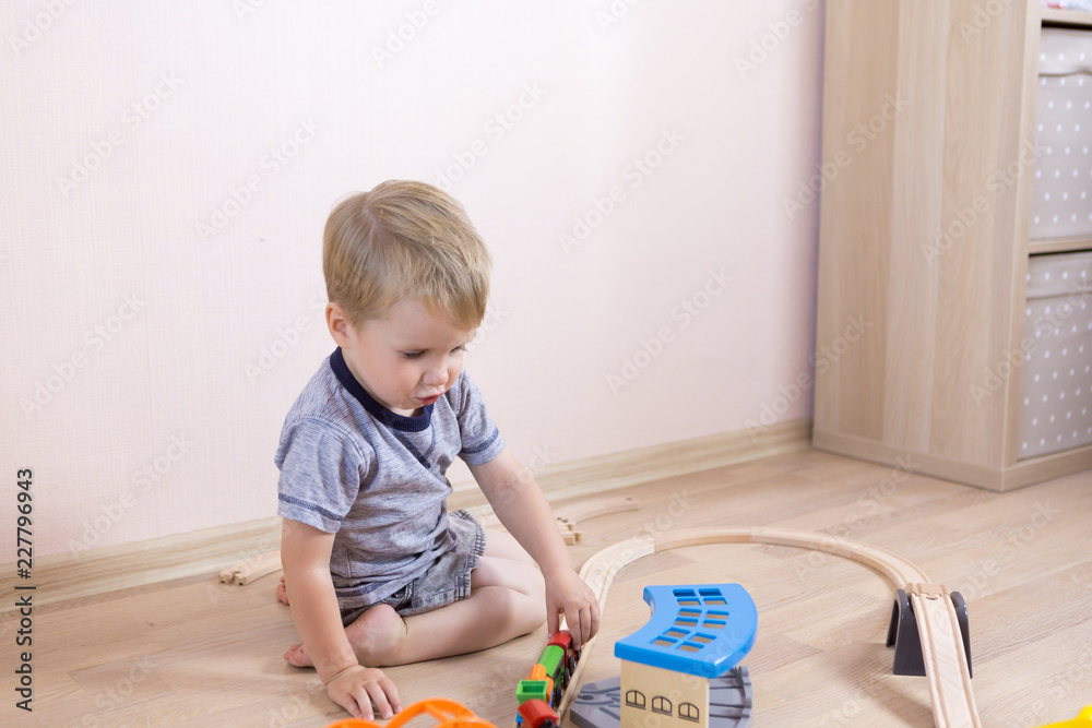 Cute kid boy playing with toy railway road at home at floor, independent children's games Cute kid boy playing with toy railway road at home at floor, independent children's games