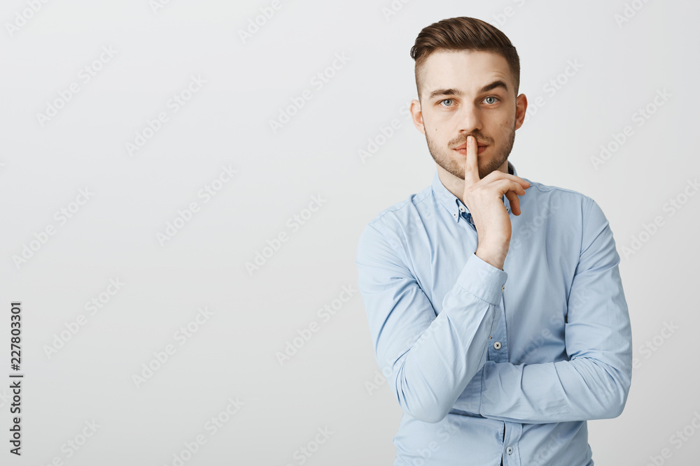 Waist-up shot of smart self-assured attractive businessman with bristle in blue office shirt making shh gesture shushing at camera with index finger over mouth telling partner keep company secret safe Waist-up shot of smart self-assured attractive businessman with bristle in blue office shirt making shh gesture shushing at camera with index finger over mouth telling partner keep company secret safe