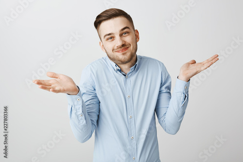 Waist-up shot of unaware carefree optimistic handsome man with bristle smiling joyfully shrugging with raised palms in questioned clueless gesture posing without no worried over gray wall