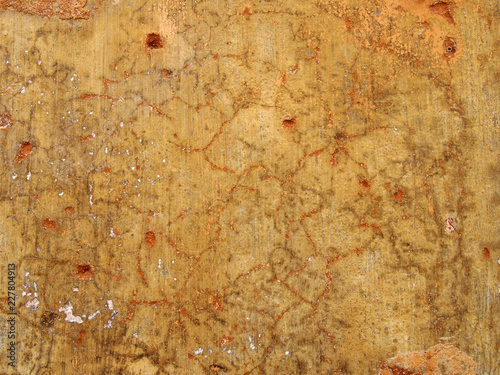 An old rough yellow ochre colored cracked faded stained painted plaster wall texture with red and orange details photo