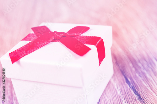 white paper gift box with thin red ribbon bow on old wood table, with copy space