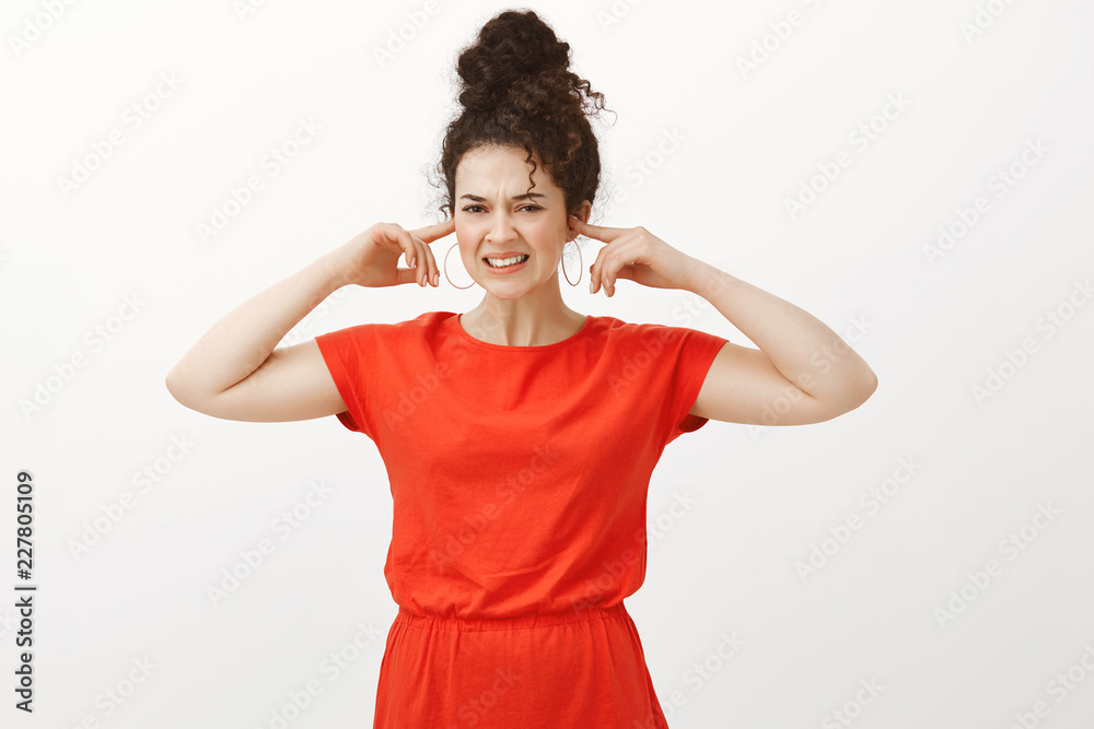 Displeased annoyed european girl with curly hair, wearing cute dress and covering ears with index fingers, grimacing and frowning from disgust, hearing disturbing sound or noise over gray wall Displeased annoyed european girl with curly hair, wearing cute dress and covering ears with index fingers, grimacing and frowning from disgust, hearing disturbing sound or noise over gray wall