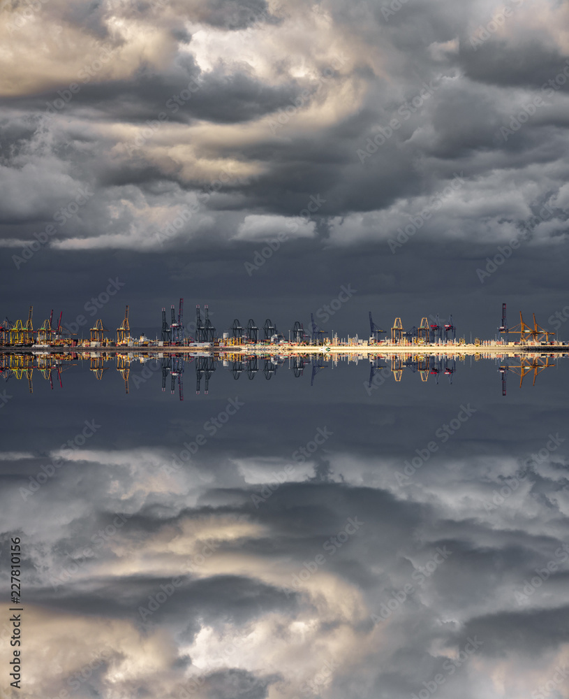 Stormy clouds over commercial port cranes with reflection