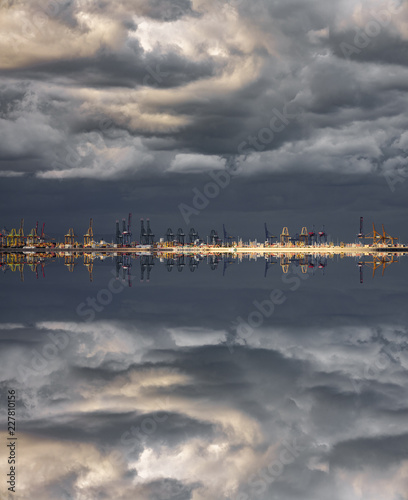 Stormy clouds over commercial port cranes with reflection