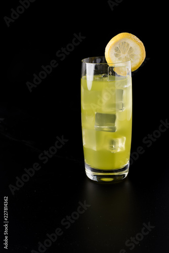 yellow cocktail with ice, slice of lemon on black background