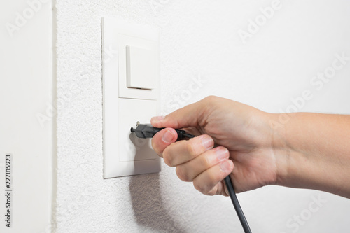 A woman's hand pulls a black cord from the socket.