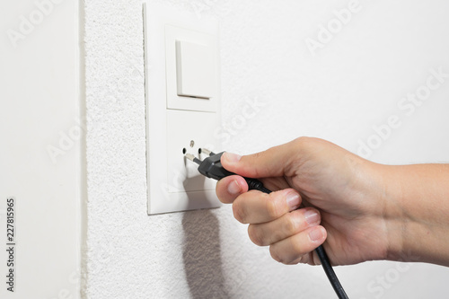 A woman's hand pulls a black cord from the socket.