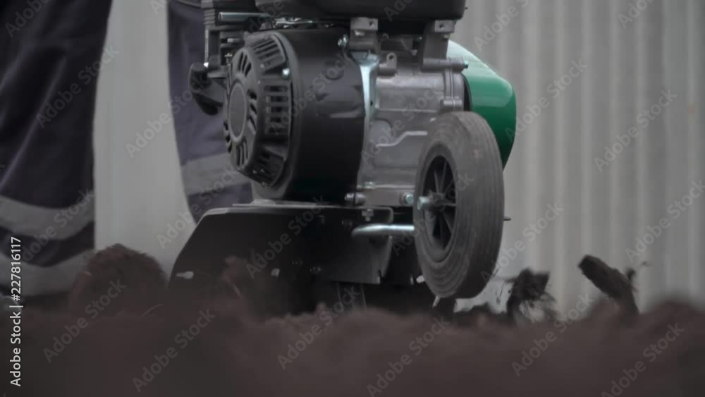 Planting potatoes under the walk-behind tractor. Man with motor-block in the garden.Cultivator digs the ground Planting potatoes under the walk-behind tractor. Man with motor-block in the garden.Cultivator digs the ground