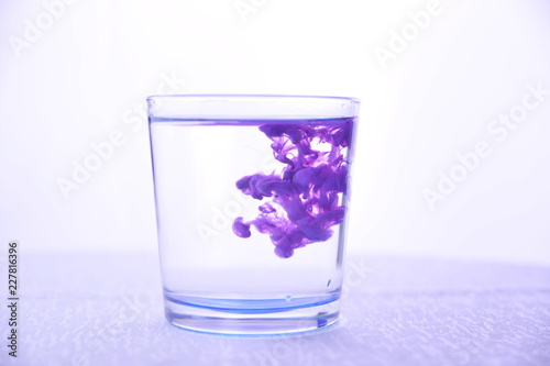 Glass with water on a white background with purple paint