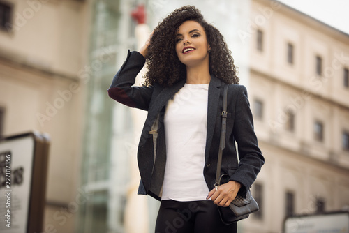 Beauty girl with curly hair in street wearing a black jacket, leggins and a bag