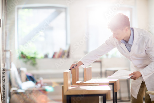 Young expert in whitecoat comparing samples of wood for new collection of furniture