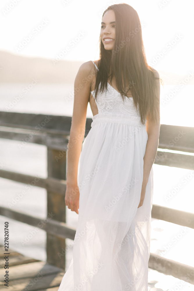 Woman smiling back while walking on a wooden pier looking down during the golden hour sunset on a warm summer day.
