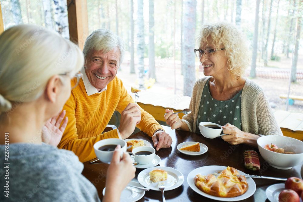 Happy senior couple looking at their friend during conversation by cup of tea in cafe