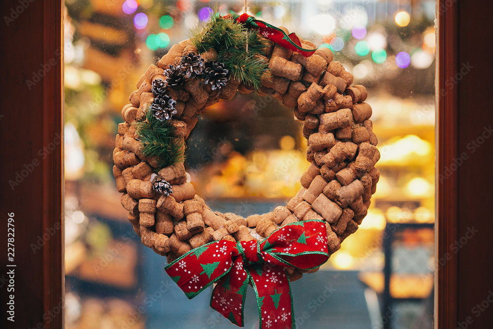 Φωτογραφία Creative christmas wreath of wine corks, pine cones and red bow on door or window   in european city street