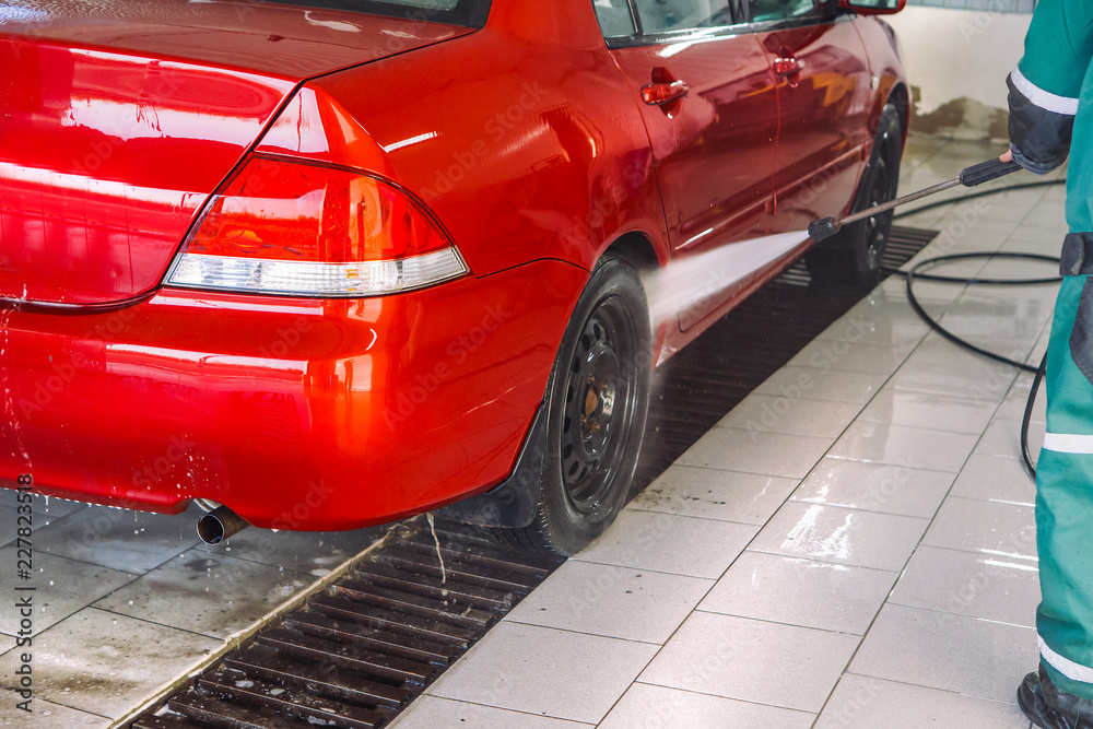Naklejka premium Red passenger car in the box at the car wash. Integrated washing under the pressure of water.