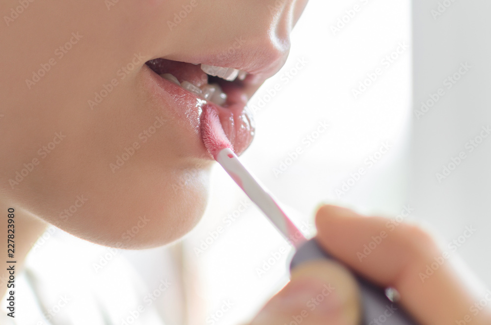 beautiful girl paints her lips with pink lip gloss