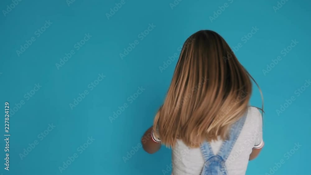 Beautiful girl with long healthy hair spinning around herself on blue background. Cute smiling girl with long hair shaking her head isolated over blue background Beautiful girl with long healthy hair spinning around herself on blue background. Cute smiling girl with long hair shaking her head isolated over blue background