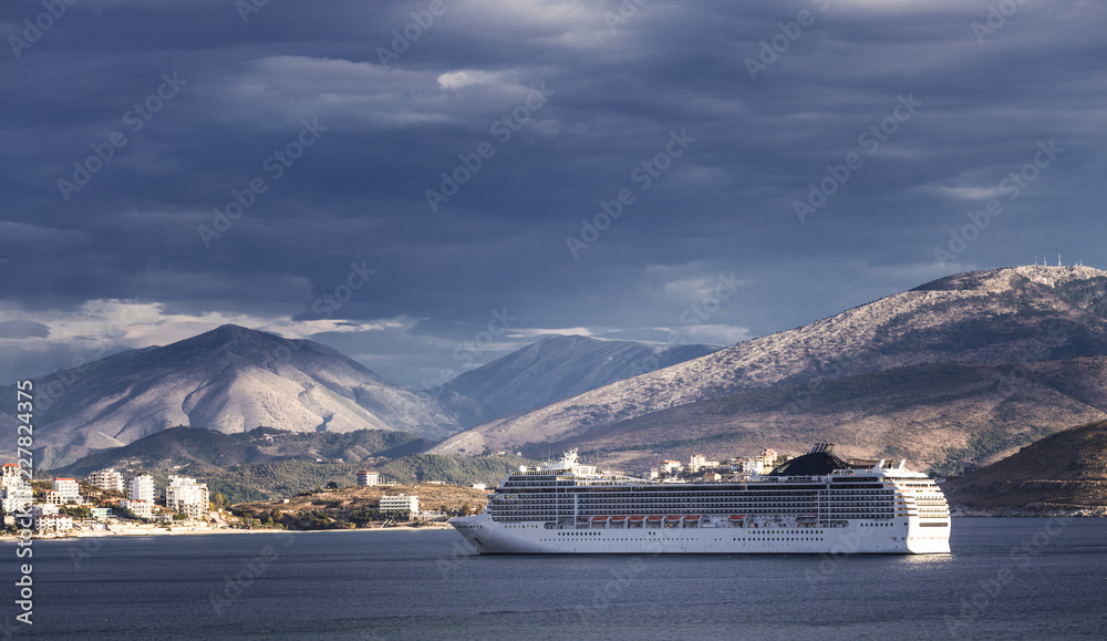 Big cruise ship sails to the sea port of Saranda, Albania. Albanian  mountains at the background. Sunset, cloudy sky. Stock Photo | Adobe Stock