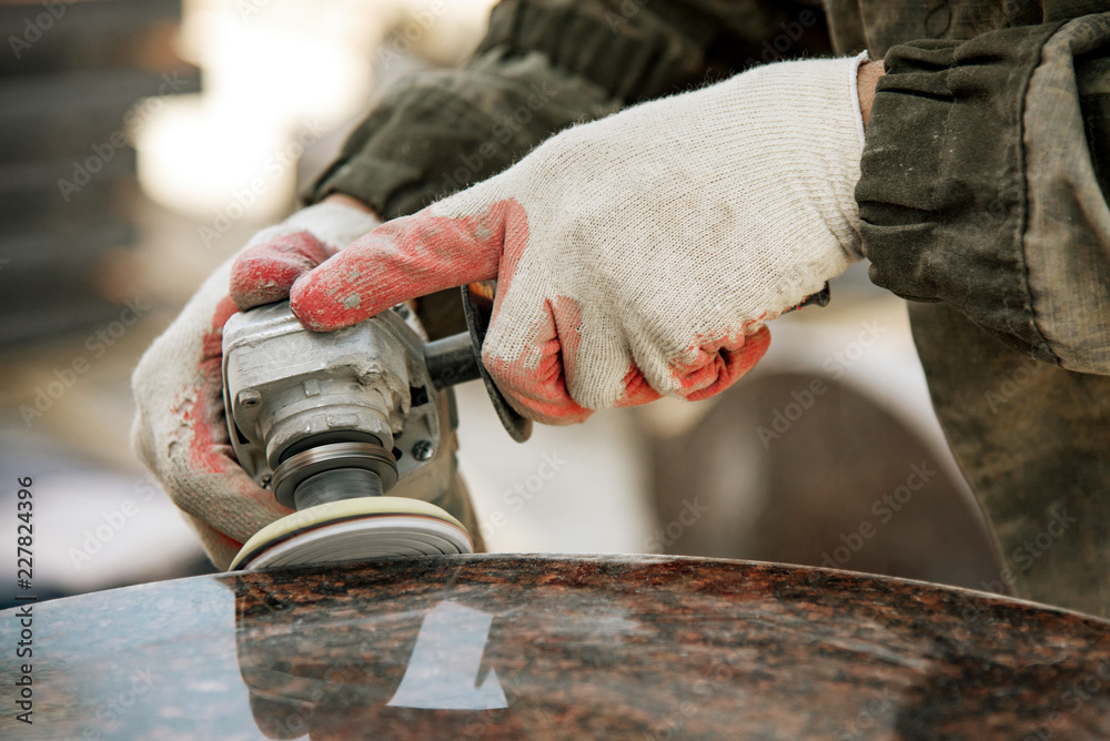 close-up worker in gloves grinds marble with an angle grinder. manufacturing of monuments. working man