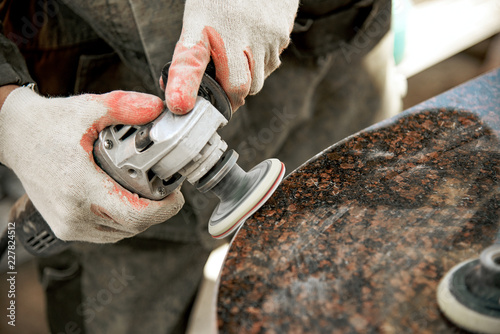 Obraz na płótnie a man in work clothes and gloves polishes a marble stone with an angle grinder. grinding stone. manufacturing of monuments. marble slab. man with a tool w salonie
