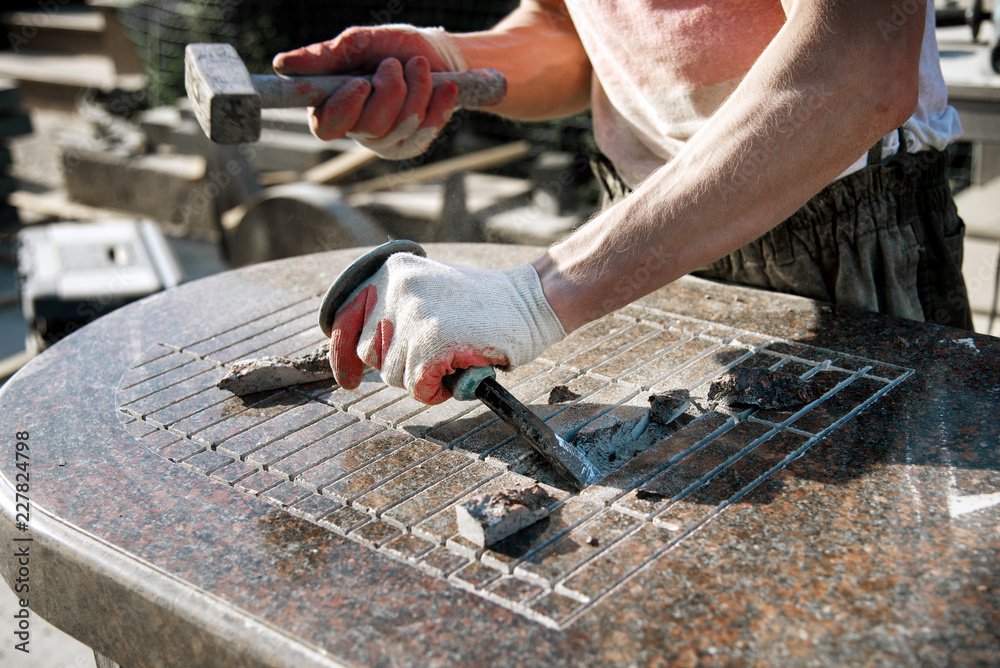 a man in gloves knocking on a chisel breaking a marble stone. stone worker. manufacturing of monuments. handwork