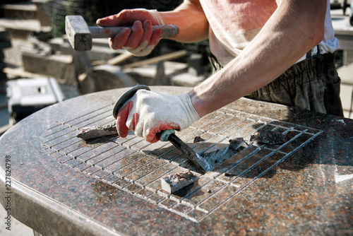 Obraz na płótnie a man in gloves knocking on a chisel breaking a marble stone. stone worker. manufacturing of monuments. handwork w salonie
