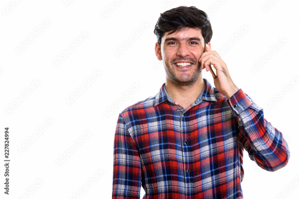 Studio shot of young happy Persian man smiling while talking on Studio shot of young happy Persian man smiling while talking on