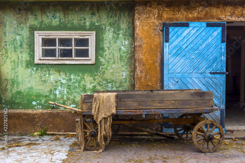 Old wooden cart in the village on the background of an old house. Large blue wooden gate.