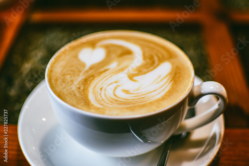 White cup of coffee with a white swan drawn on a brown coffee foam. Elegant coffee art. Concept background of cafe, rest, leisure, and romantic settings