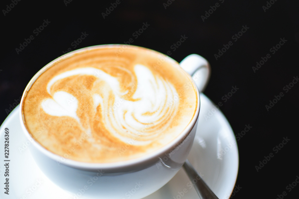 White cup of cappuccino with a white swan drawn on a brown coffee foam. Elegant coffee art. Concept background of cafe, rest, leisure, and romantic settings. View from above. Deep black background White cup of cappuccino with a white swan drawn on a brown coffee foam. Elegant coffee art. Concept background of cafe, rest, leisure, and romantic settings. View from above. Deep black background