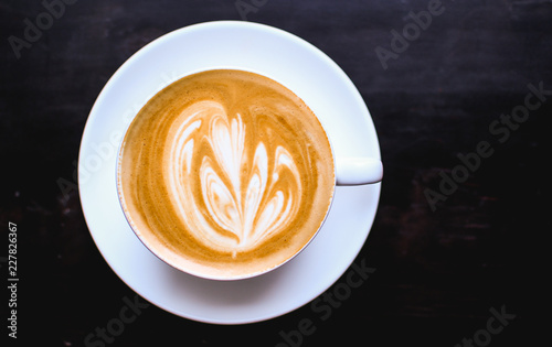 White cup of cappuccino with an abstract drawing on a brown coffee foam. Elegant coffee art. Concept background of cafe  rest  leisure  and romantic settings. View from above. Deep black background