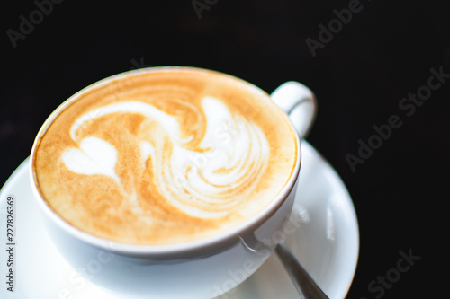 White cup of cappuccino with a white swan drawn on a brown coffee foam. Elegant coffee art. Concept background of cafe, rest, leisure, and romantic settings. View from above. Deep black background