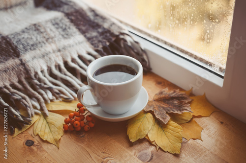 Autumn background. A cup of hot coffee, autumn yellow leaves on a wooden surface. Rain