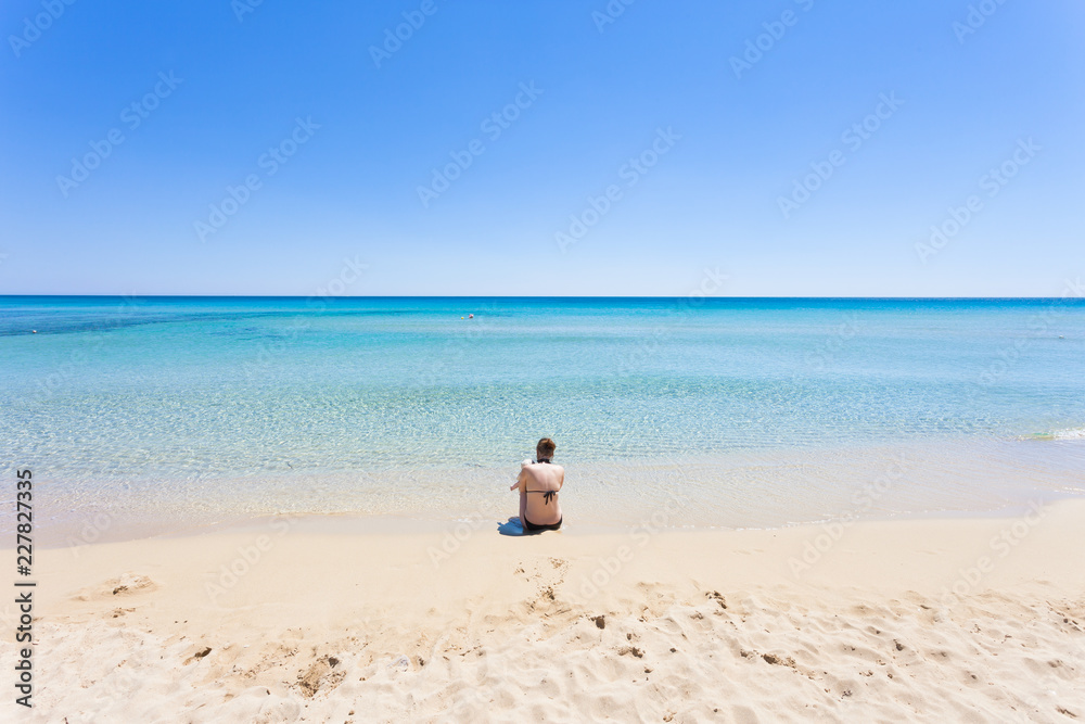 Lido Venere, Apulia - A young mother sitting on the beach looking towards the horizon Lido Venere, Apulia - A young mother sitting on the beach looking towards the horizon