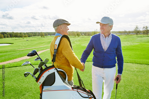 Two friendly mature golf players shaking hands while greeting one another before game