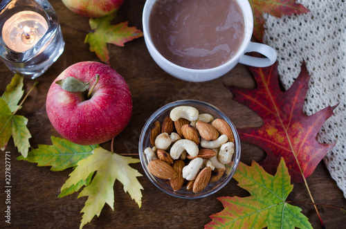 A cup of hot cocoa with knitted blanket, nuts, apples and autumn leaves. Thanksgiving day concept.