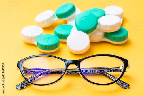 Glasses on the background of a pile of containers for storing contact lenses on a yellow background. Concept - glasses against lenses