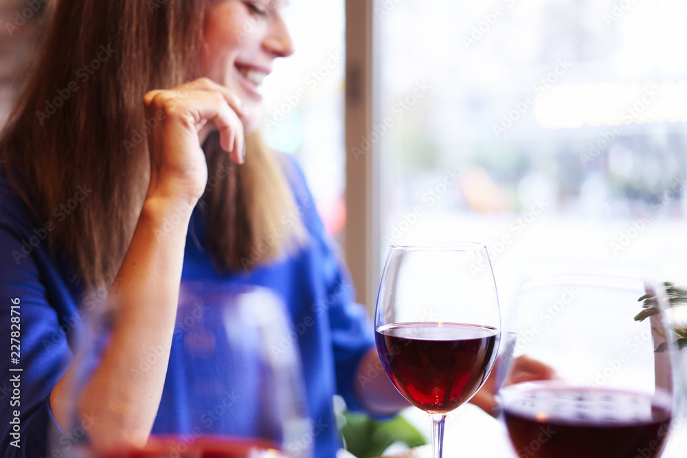 Woman drinking red wine with friends in cafe, focus on glass near window. Vocation holidays bar concept. Woman drinking red wine with friends in cafe, focus on glass near window. Vocation holidays bar concept.