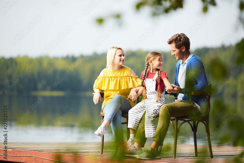 Cute little girl talking to her dad while family sitting by riverside on summer weekend Cute little girl talking to her dad while family sitting by riverside on summer weekend
