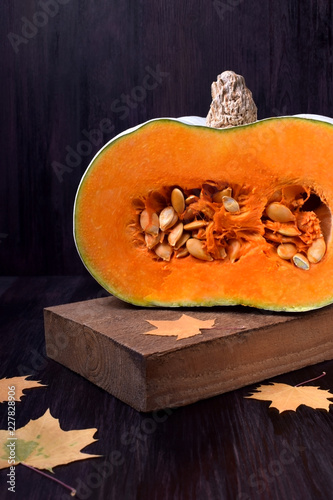 Fotografie Half of a pumpkin with orange flesh on a wooden board surrounded by dry maple le