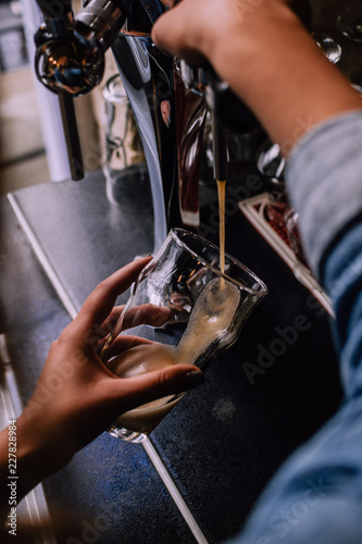 Girl pouring a pint of dark beer in a craft beer pub. Local pub. Shiny beer taps on the background. Bright sunny afternoon. Look from behind.