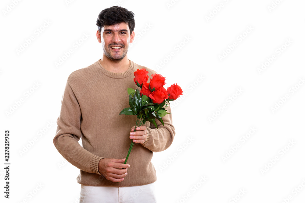 Studio shot of young happy Persian man smiling while holding red Studio shot of young happy Persian man smiling while holding red