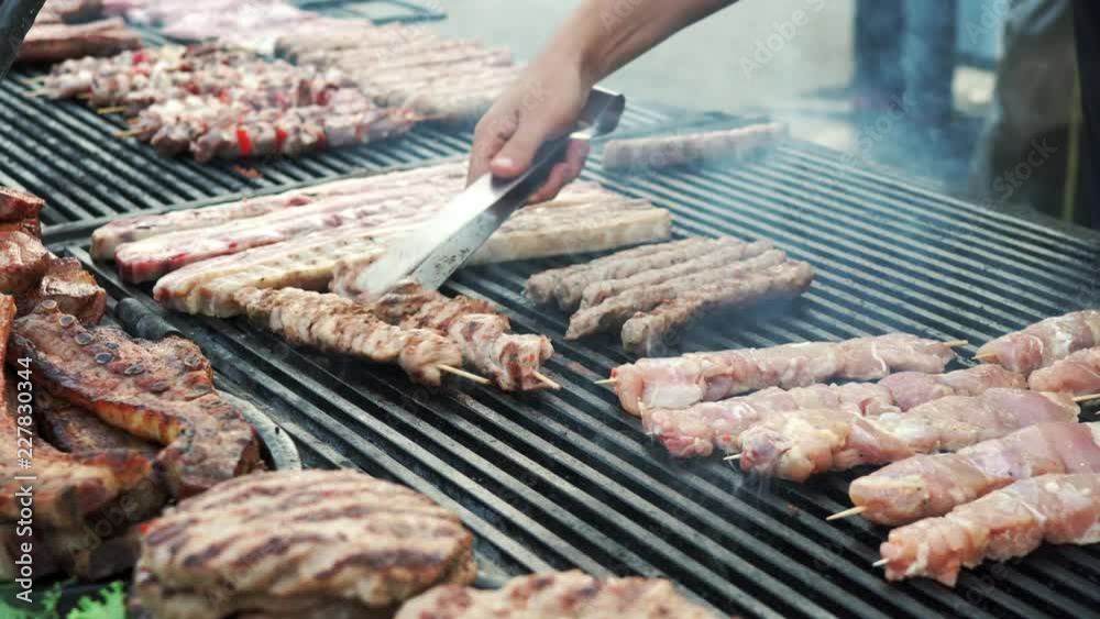 Market town food. Festival of meat and wine on the main square of the city. Grilled meat with smoke. The chef fries meat, kebabs, kebabs on a large hot grill and overturns the ready meal