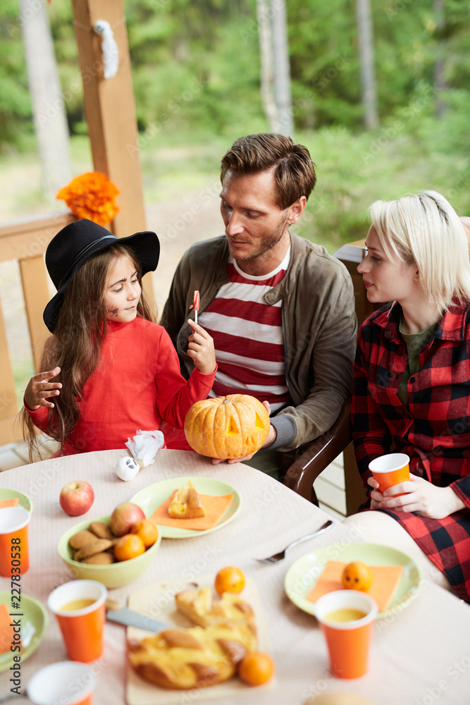 Family of young parents and their adorable daughter sitting by halloween table and discussing symbols of holiday