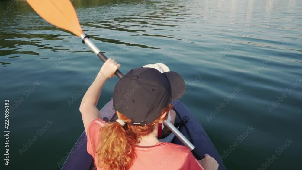Slow motion slide young woman paddling on an inflatable kayak on the water of a large mountain lake against a beautiful orange sunset. Family Sports Weekend